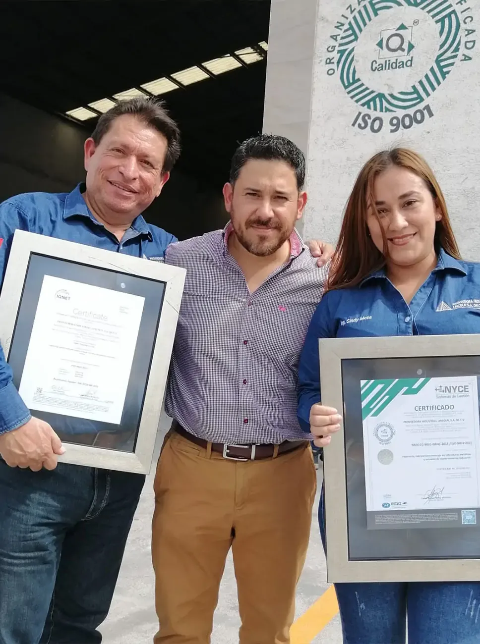 Personas sonrientes sostienen certificados enmarcados, celebrando la exitosa implementación de normas ISO 9001.