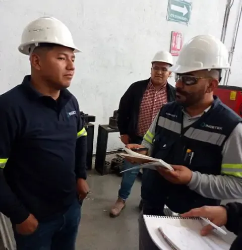 Trabajadores con cascos de seguridad revisando documentos en un industria, preparándose para consultoría de normas ISO.