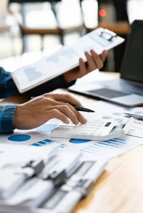 Una persona usando una calculadora sobre reportes financieros y gráficos durante la ejecución de auditorías internas.