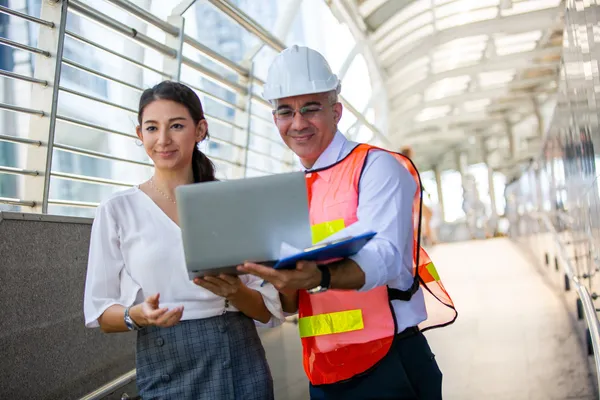 Dos profesionales, un hombre con casco blanco y una mujer, revisan un portátil simbolizando la gestión de seguridad ISO 45001.