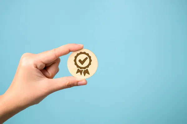 Una mano sostiene una ficha de madera con un sello, simbolizando la certificación obtenida con un Diplomado en Normas ISO.