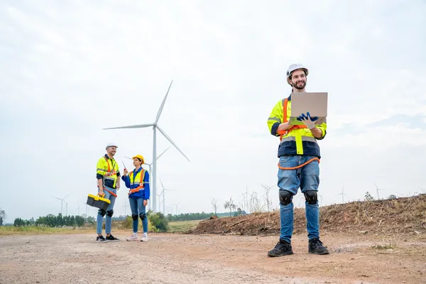 Trabajadores, uno sostiene una laptop en parque eólico gestiona datos del equipo para la certificación ISO 14001.